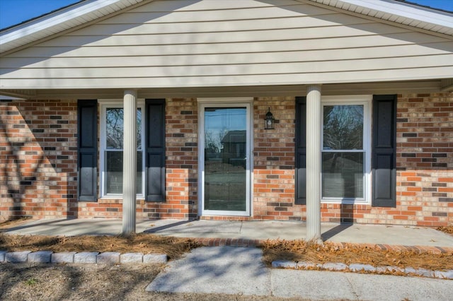 view of exterior entry with a porch and brick siding