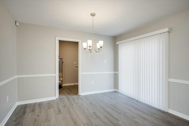 spare room with an inviting chandelier, water heater, and light wood-type flooring