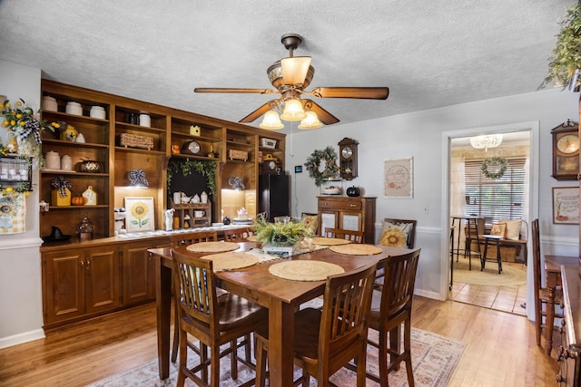 dining space with a textured ceiling, ceiling fan with notable chandelier, and light wood-type flooring