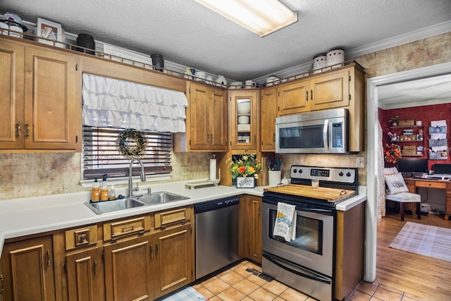 kitchen with appliances with stainless steel finishes, ornamental molding, a textured ceiling, sink, and light tile patterned flooring