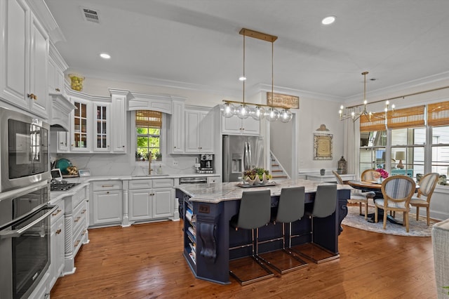 kitchen featuring stainless steel appliances, white cabinets, a kitchen island, ornamental molding, and a sink