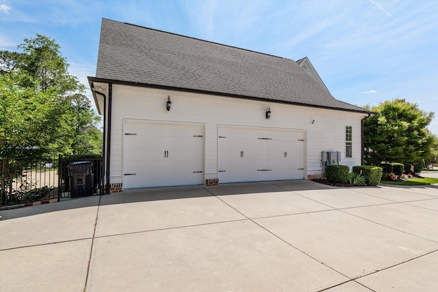 view of property exterior with fence, a garage, roof with shingles, and concrete driveway