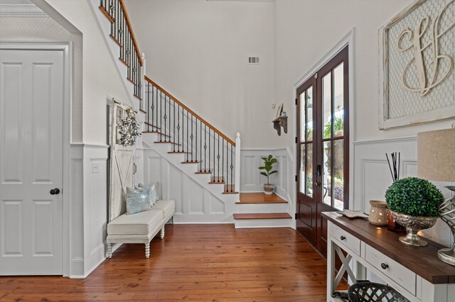 entrance foyer with a decorative wall, wood-type flooring, a high ceiling, stairway, and french doors