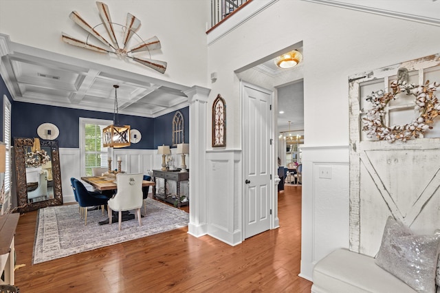 dining space with a chandelier, a decorative wall, coffered ceiling, wood finished floors, and ornamental molding