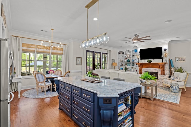 kitchen with blue cabinets, freestanding refrigerator, a ceiling fan, a fireplace, and light wood-style floors