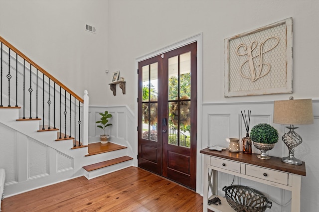 entryway featuring wood finished floors, french doors, stairway, wainscoting, and a decorative wall