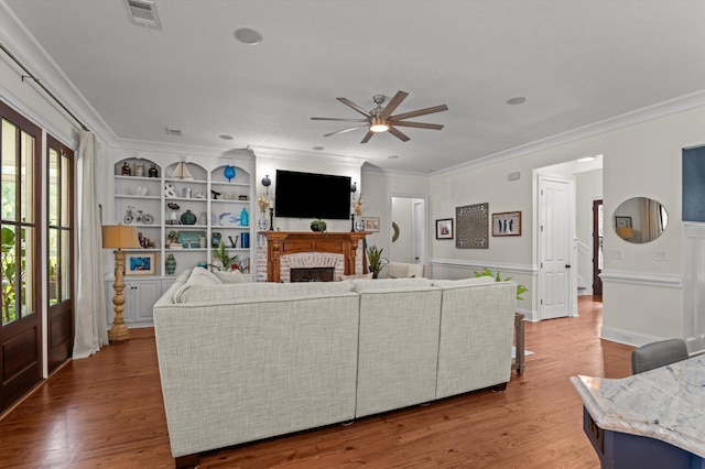living area featuring ornamental molding, a ceiling fan, a fireplace, wood finished floors, and built in features