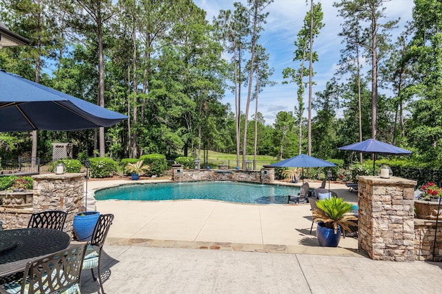 view of swimming pool with a patio area, fence, and view of wooded area