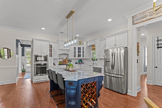 kitchen featuring appliances with stainless steel finishes, white cabinets, a sink, healthy amount of natural light, and ornamental molding