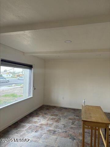 spare room with beamed ceiling, baseboards, and stone finish flooring