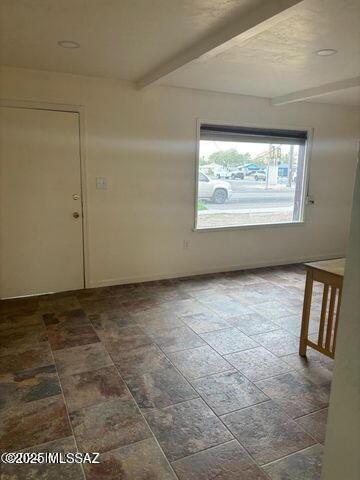 unfurnished room with baseboards, beam ceiling, and stone finish floor