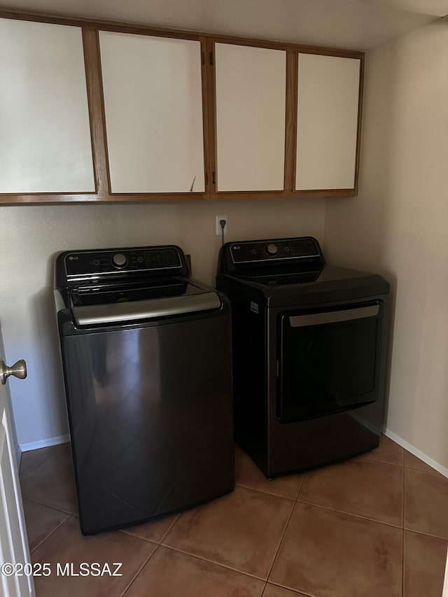 clothes washing area with tile patterned floors, washing machine and clothes dryer, and cabinets