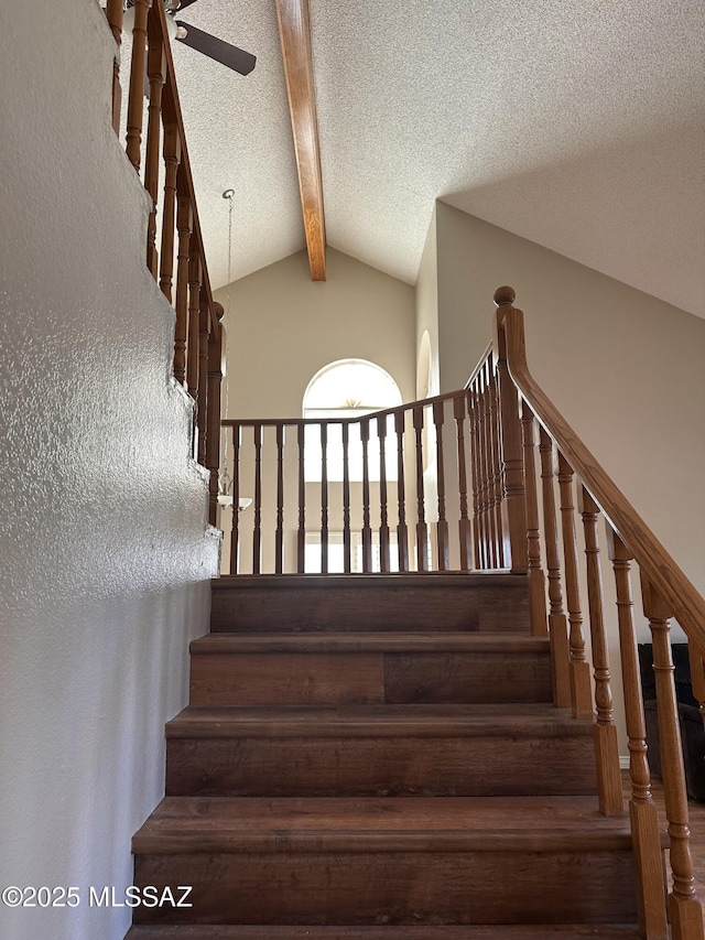 stairs with a textured ceiling, ceiling fan, and vaulted ceiling with beams