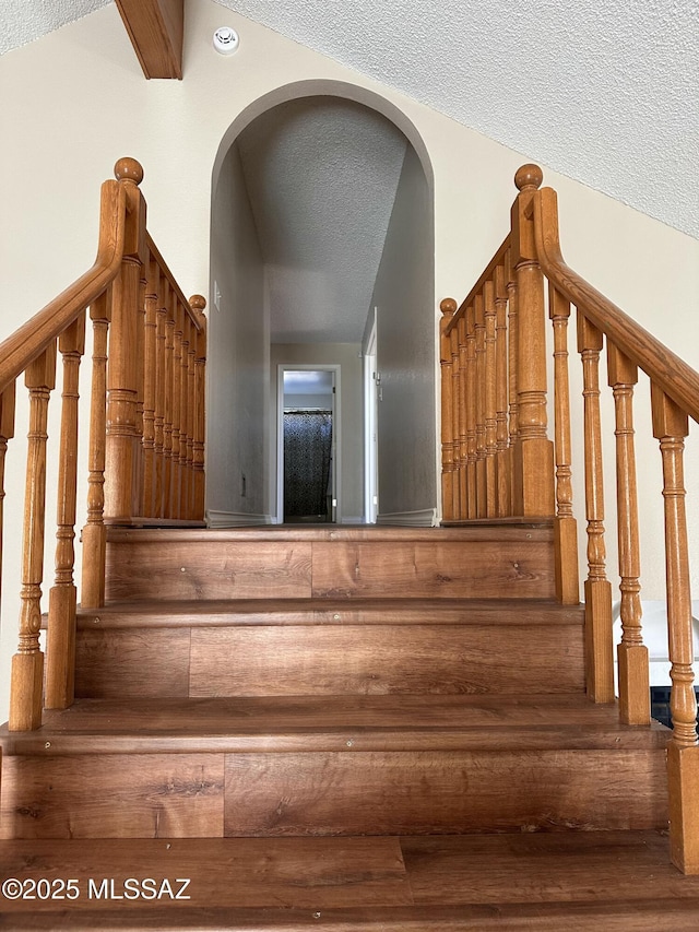 stairway featuring a textured ceiling and beamed ceiling