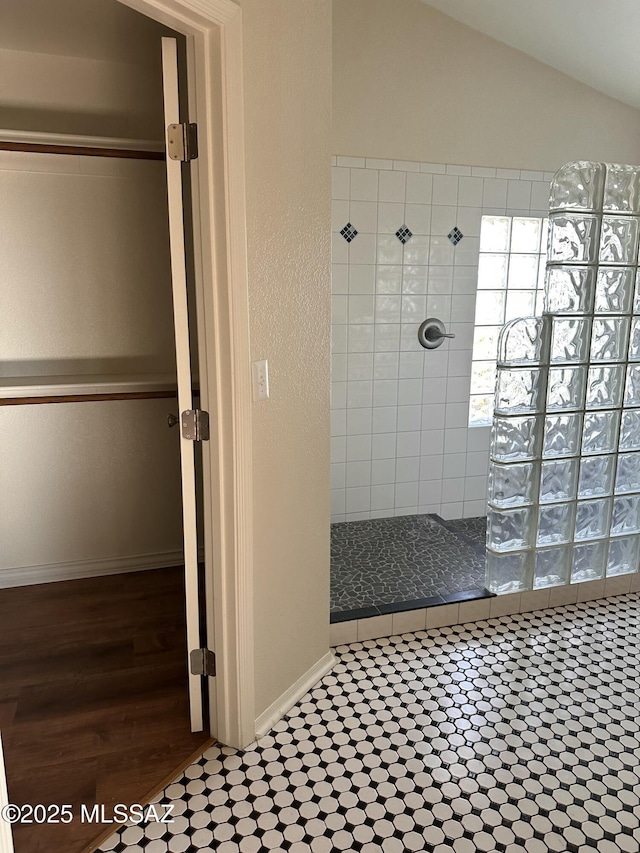 bathroom with lofted ceiling, tile patterned flooring, and a tile shower