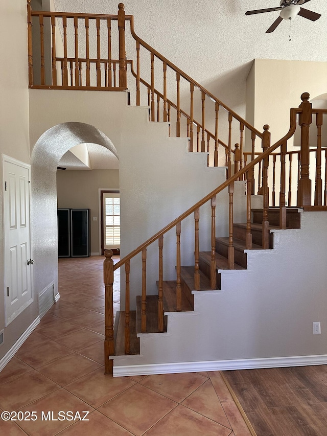 staircase with ceiling fan, tile patterned floors, and a towering ceiling