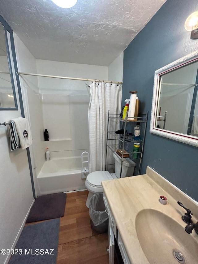 full bathroom with toilet, hardwood / wood-style floors, vanity with extensive cabinet space, shower / bath combination with curtain, and a textured ceiling