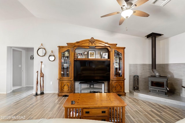 living room with ceiling fan, vaulted ceiling, a wood stove, and light wood-type flooring