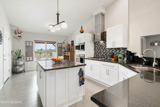 kitchen with sink, hanging light fixtures, wall chimney exhaust hood, white cabinetry, and a center island