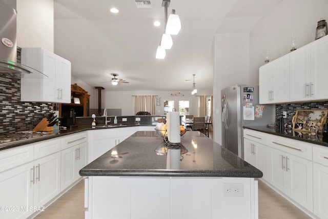 kitchen featuring a center island, ceiling fan, decorative light fixtures, sink, and wall chimney exhaust hood