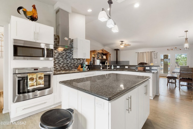 kitchen featuring stainless steel appliances, decorative light fixtures, a center island, ceiling fan, and wall chimney exhaust hood