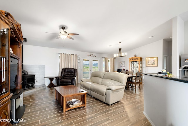 living room with lofted ceiling, a wood stove, and ceiling fan with notable chandelier