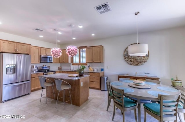 kitchen featuring hanging light fixtures, light stone counters, appliances with stainless steel finishes, and a center island