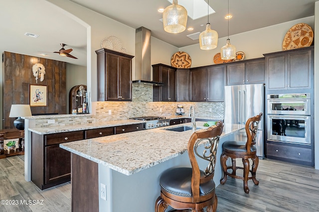 kitchen featuring ceiling fan, appliances with stainless steel finishes, backsplash, wall chimney exhaust hood, and decorative light fixtures