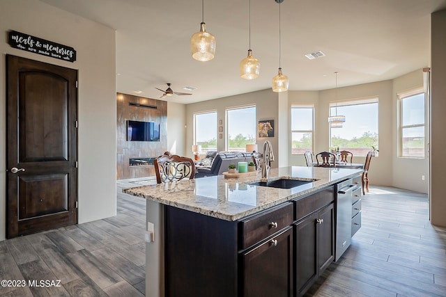 kitchen featuring light hardwood / wood-style floors, decorative light fixtures, ceiling fan, a kitchen island with sink, and sink