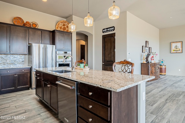 kitchen with decorative light fixtures, backsplash, light hardwood / wood-style flooring, an island with sink, and light stone counters