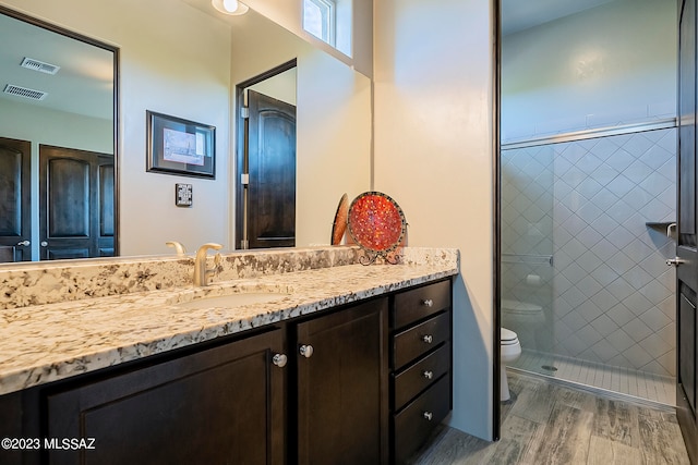 bathroom featuring toilet, tiled shower, hardwood / wood-style floors, and vanity with extensive cabinet space