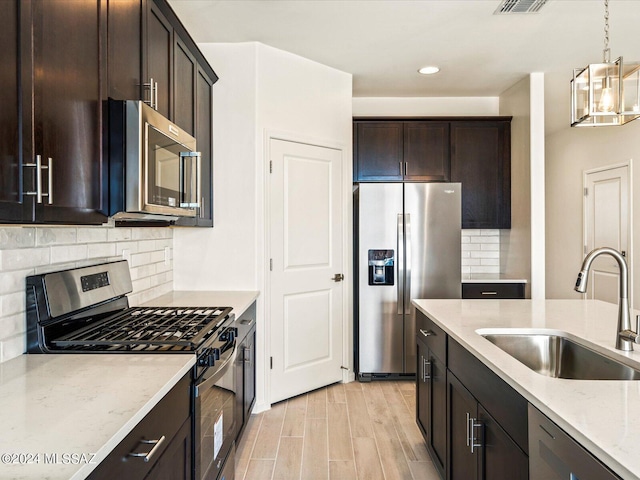 kitchen featuring sink, stainless steel appliances, light stone countertops, decorative light fixtures, and light wood-type flooring