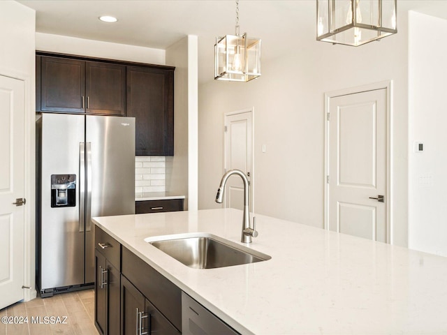 kitchen featuring pendant lighting, sink, dark brown cabinetry, light stone counters, and stainless steel refrigerator with ice dispenser