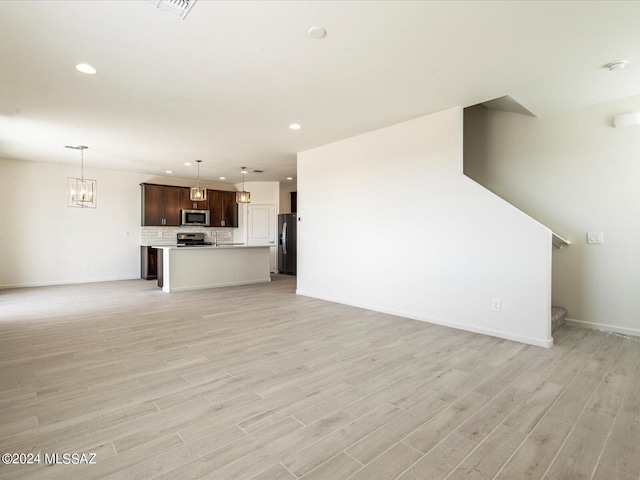 unfurnished living room featuring an inviting chandelier and light wood-type flooring