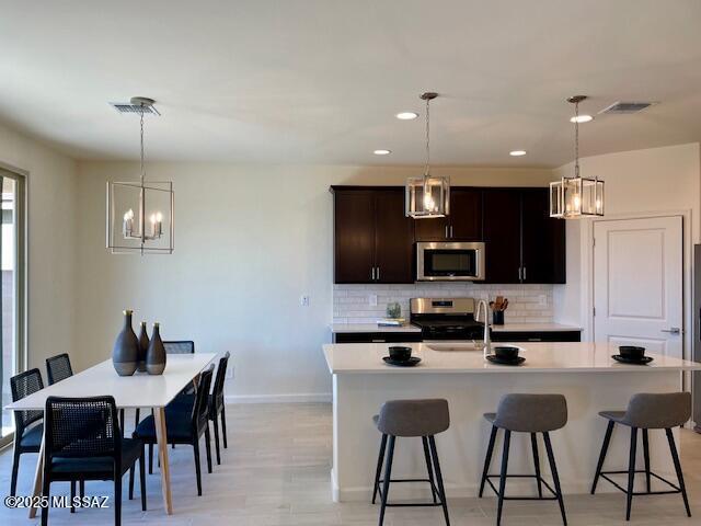 kitchen featuring pendant lighting, decorative backsplash, dark brown cabinets, and stainless steel appliances