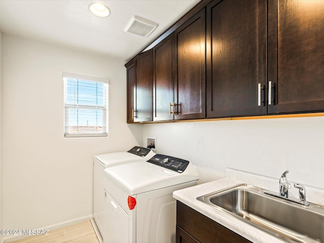 clothes washing area featuring washer and dryer, sink, light hardwood / wood-style floors, and cabinets