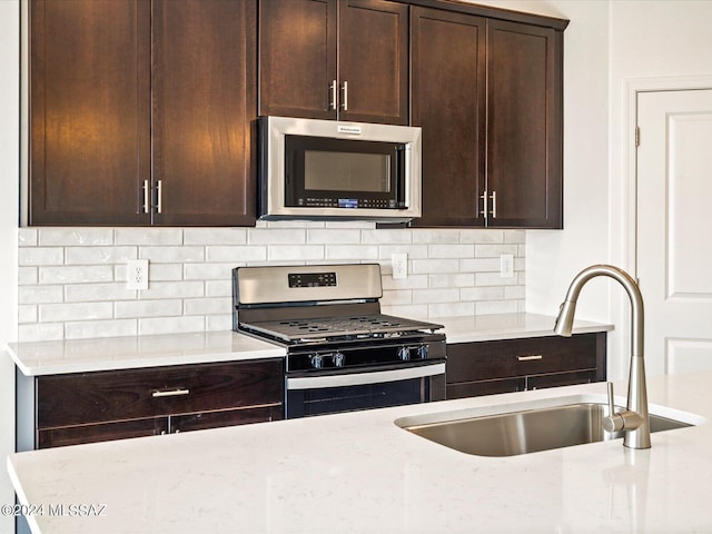 kitchen with appliances with stainless steel finishes, sink, decorative backsplash, dark brown cabinetry, and light stone countertops