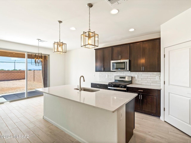 kitchen featuring sink, stainless steel appliances, dark brown cabinetry, a center island with sink, and decorative backsplash