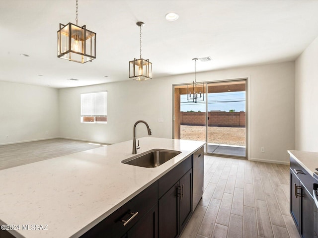 kitchen featuring decorative light fixtures, dishwasher, sink, and light wood-type flooring