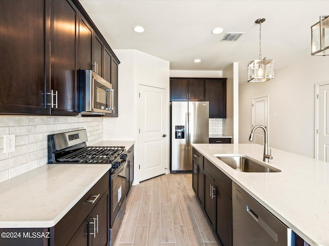 kitchen with sink, decorative backsplash, hanging light fixtures, stainless steel appliances, and light wood-type flooring