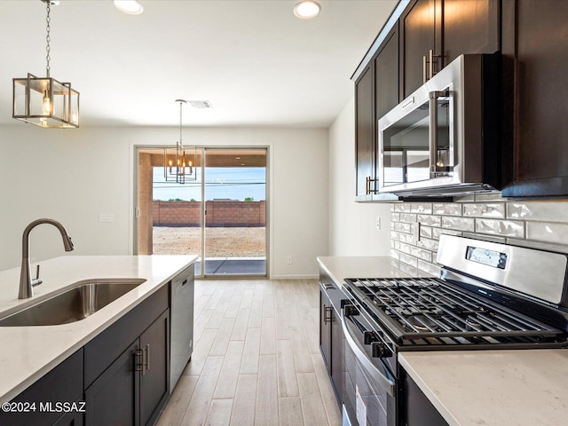 kitchen featuring sink, decorative light fixtures, appliances with stainless steel finishes, light hardwood / wood-style floors, and backsplash