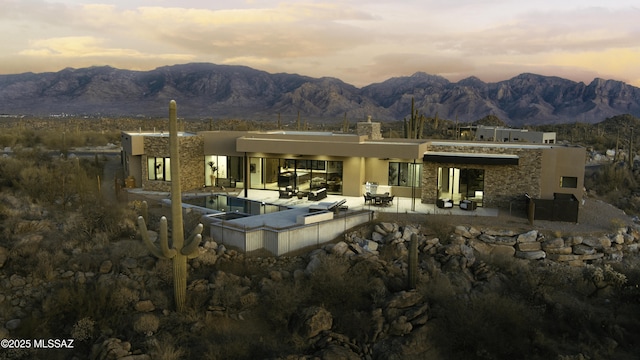 back of property featuring a mountain view, an outdoor pool, stone siding, stucco siding, and a patio area