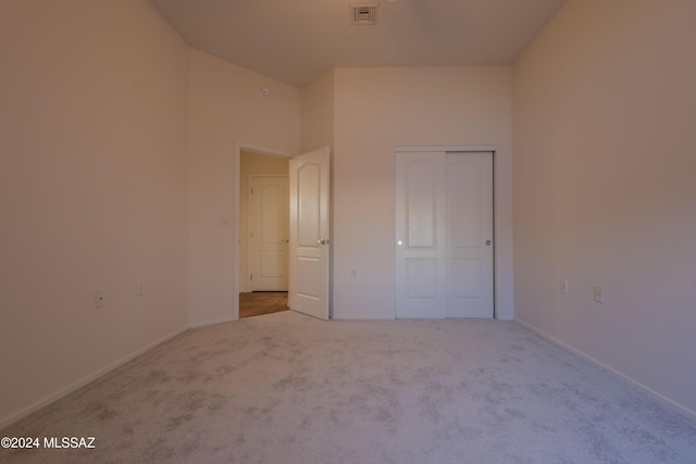 unfurnished bedroom with high vaulted ceiling, a closet, and carpet flooring