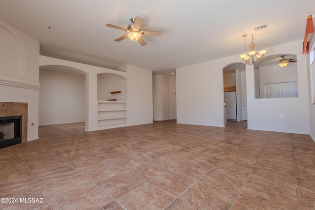 unfurnished living room featuring built in shelves, a fireplace, and ceiling fan with notable chandelier