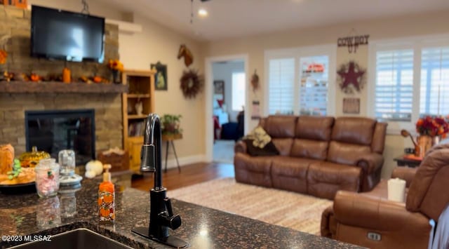 living room with a stone fireplace, vaulted ceiling, sink, and hardwood / wood-style flooring