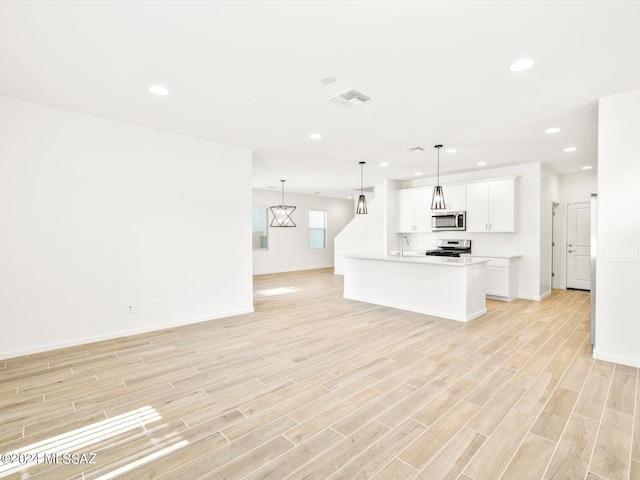 kitchen with white cabinetry, an island with sink, appliances with stainless steel finishes, pendant lighting, and light hardwood / wood-style flooring