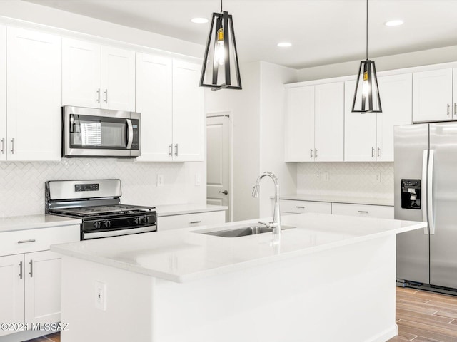 kitchen with light wood finished floors, a center island with sink, appliances with stainless steel finishes, white cabinetry, and a sink