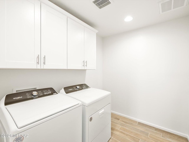 clothes washing area with wood finish floors, visible vents, cabinet space, and separate washer and dryer