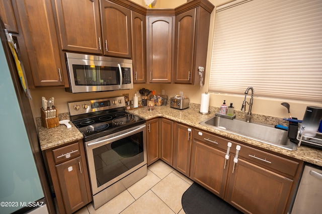 kitchen with light tile patterned flooring, sink, appliances with stainless steel finishes, and light stone counters