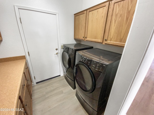 clothes washing area featuring washing machine and dryer, light hardwood / wood-style flooring, and cabinets